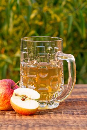 Glass goblet of apple cider and apples on wooden boards with leaves of a treeの写真素材