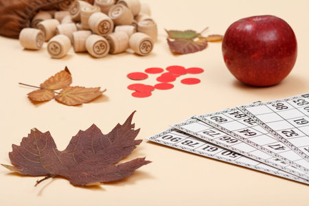 Wooden lotto barrels with open bag, dry autumn leaf, red apple and game cards on beige background....