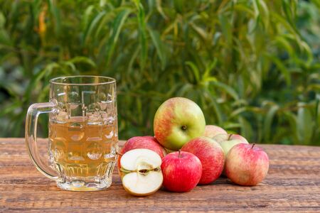 Glass goblet of apple cider and harvested apples on old wooden boards with leaves of tree on the background. Just picked fruits. Organic drinks and food.の写真素材