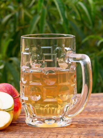 Glass goblet of apple cider and harvested apples on wooden boards with green leaves of tree on the background.の写真素材