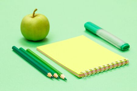 Color pencils, notebook, felt pen and apple on green background. Back to school concept. School supplies. Shallow depth of field.の写真素材