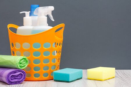 Plastic basket with bottles of dishwashing liquid and tile cleaner, detergent for microwave ovens and stoves, sponges and garbage bags on gray background. Washing and cleaning concept.の写真素材