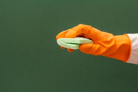 Woman's hand in orange protective glove with sponge on the green background. Washing and cleaning concept.の写真素材