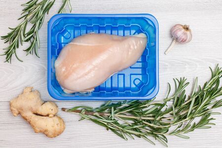 Fresh raw chicken breast or fillet in a plastic container with ginger root, garlic and rosemary on a wooden background. Top view.の写真素材