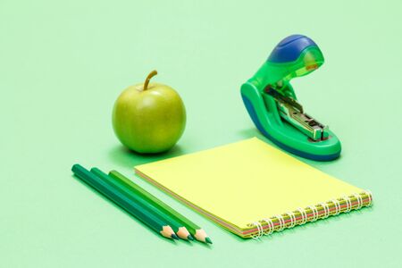 Color pencils, notebook, apple and stapler on green background. Back to school concept. School supplies. Shallow depth of field.の写真素材