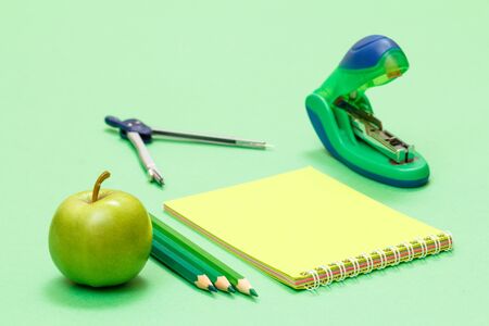 Compass, color pencils, notebook, apple and stapler on green background. Back to school concept. School supplies. Shallow depth of field.の写真素材