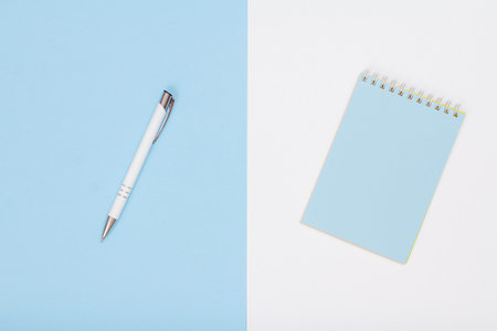 School supplies. Notebook and pen on white and blue background. Top view. Back to school concept.