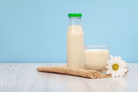 Bottle and glass of fresh cow milk with chamomile flower on sackcloth and blueの写真素材