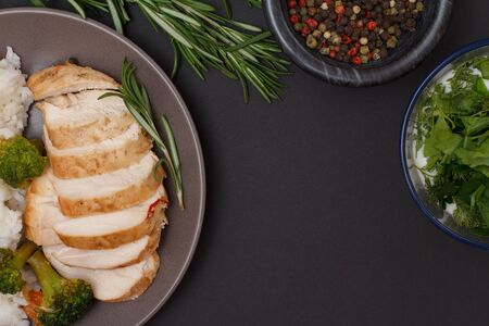 Baked chicken breasts or fillet on plate with rosemary, glass bowls with sauce and allspice berries on black background. Top view.の写真素材