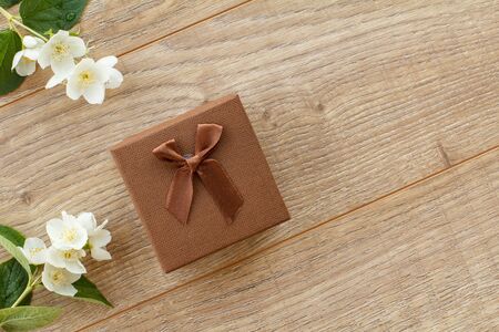 Brown gift box with beautiful jasmine flowers on the wooden background. Concept of giving a gift on holidays. Top view with copy space.の写真素材
