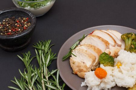 Baked chicken breasts or fillet on plate, rosemary, bowls with sauce and allspice berries on blackの写真素材