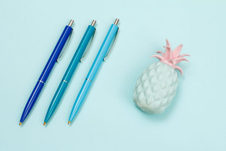 Three pens and plastic figure of a pineapple on a blue