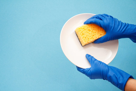 Women's hands in protective gloves with white plate and blue sponge on blue