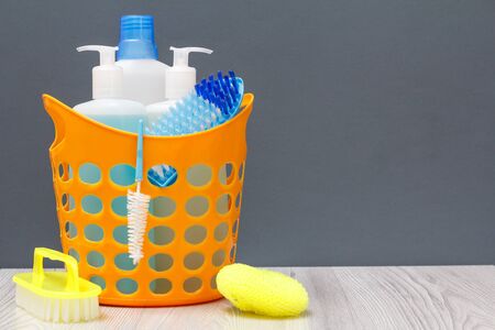Plastic basket with bottles of dish washing liquid, glass and tile cleaner, detergent for microwave ovens and stoves with brush and sponges on grayの写真素材