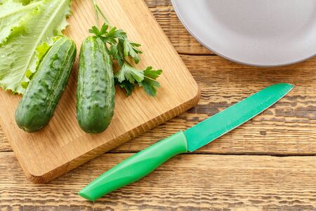 Just picked cucumbers and green salad on cutting board, knife and plate on old wooden boards.の写真素材