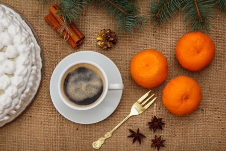Biscuit cake decorated with whipped cream, cup of coffee, fork, oranges, star anise and cinnamon with branch of spruce on sackcloth. Top view.の写真素材
