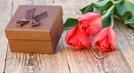 Brown gift box with beautiful red tulips on the wooden boards. Concept of giving a gift on holidays.の写真素材