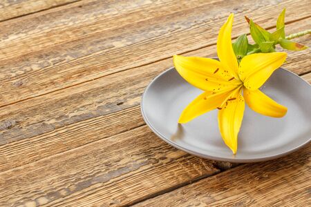Porcelain plate and beautiful yellow lily on old wooden boards. Concept of giving a gift on any holidays. Top view.の写真素材