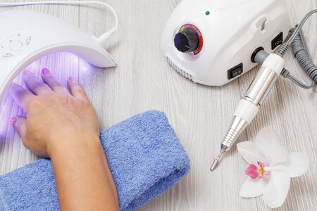 Milling cutter and led UV lamp with woman's hand on gray wooden background. A set of cosmetic tools for professional hardware manicure. Top viewの写真素材