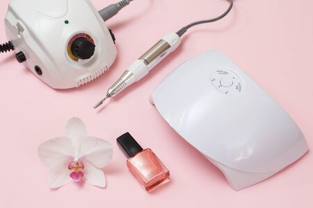 Milling cutter, led UV lamp, nail polishes and orchid flower on a pink background. A set of cosmetic tools for professional hardware manicure. Top view.の写真素材