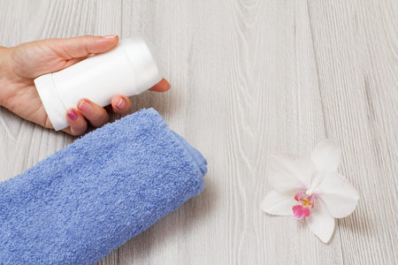 Deodorant in woman's hand, towel with orchid on a gray wooden background with copy space. Women...