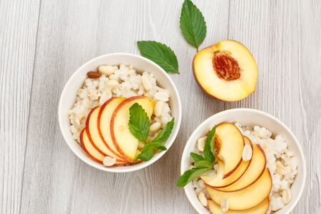 Porcelain bowls with sorghum porridge, cut peaches, cashew nuts, almond and mint leaves on gray wooden boards. Vegan gluten-free sorghum salad with fresh fruits. Top view.の写真素材