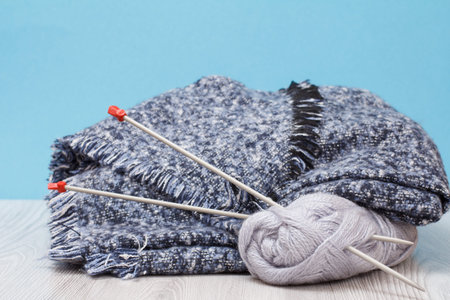 Scarf and skeins of yarn with metal knitting needles on gray boards and a blue