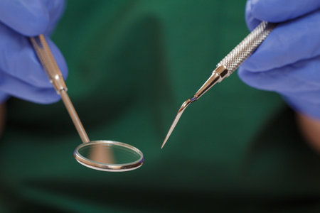 Close-up view of dentist's hands in rubber gloves with probe and mouth mirror. Shallow depth of...