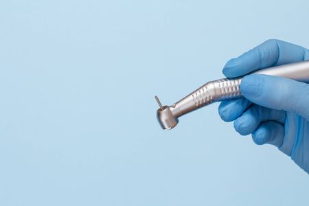 Dentist's hand in a rubber glove with high-speed dental hand piece on blueの写真素材