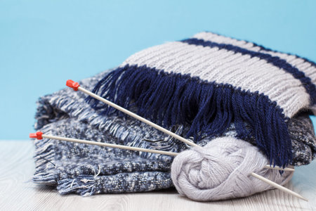 Scarfs and skeins of yarn with metal knitting needles on gray boards and a blue background. Knitting...