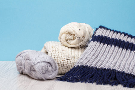 Pullover, scarf and skeins of yarn with metal knitting needles on gray boards and a blue background....