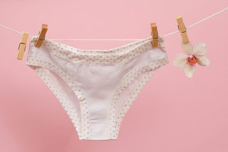 New, white panties on clothesline with clothespins and orchid flower in pink background. Woman...