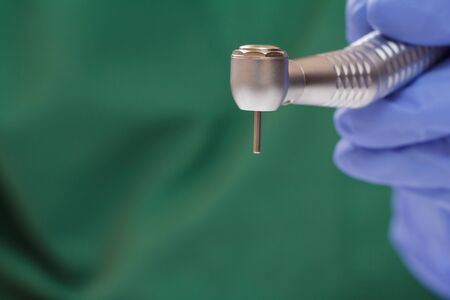 Close-up dentist's hand in a latex gloves with high-speed dental handpiece on blurred background. Medical tools concept. Shallow depth of fiel.の写真素材