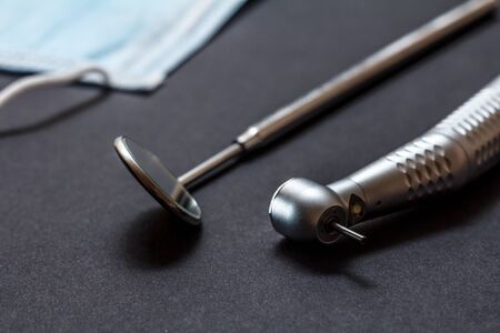 Set of metal dental instruments for dental treatment. High-speed dental handpiece, dental mirror and mask on blackの写真素材