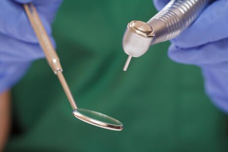 Close-up dentist's hands in latex gloves with mouth mirror and high-speed dental handpiece on blurredの写真素材