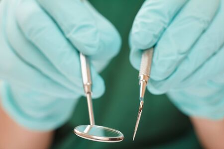 Close-up view of dentist's hands in latex gloves with probe and metal mouth mirror. Shallow depth of field. Medical tools concept.の写真素材
