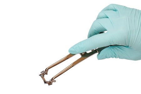 Dentist's hand in a latex glove with dental tongs and clasp on white isolated background. Medical tools concept.の写真素材