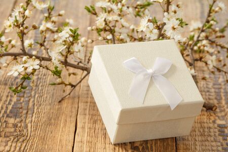 Gift box with branches of flowering cherry tree on the wooden background. Concept of giving a gift on holidays.の写真素材