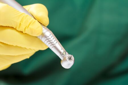 Dentist's hand in a yellow latex glove with new high-speed dental handpiece on blurred background. Medical tools concept.の写真素材