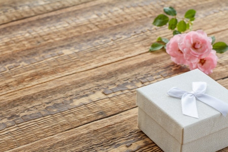 White gift box on old wooden boards decorated with pink roses. Top view with copy space.