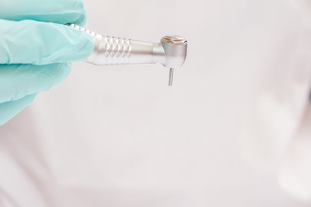 Close-up dentist's hand in a latex glove with high-speed dental hand piece on blurred