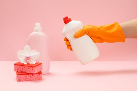 Woman's hand in a rubber protective glove with a bottle of dishwashing liquid on the pink background. Washing and cleaning concept.の写真素材