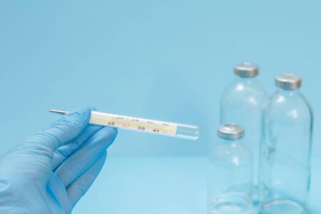 Close-up view of female doctor's hand in a latex glove holding a glass mercury thermometer with blurred glass bottlesの写真素材