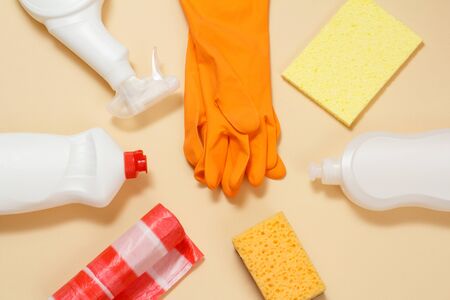 Orange protective gloves with plastic bottles of washing and cleaning liquids on the beige background. Top view.の写真素材