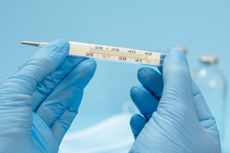 Close-up view of female hands in blue latex gloves holding a glass mercury thermometer with a...