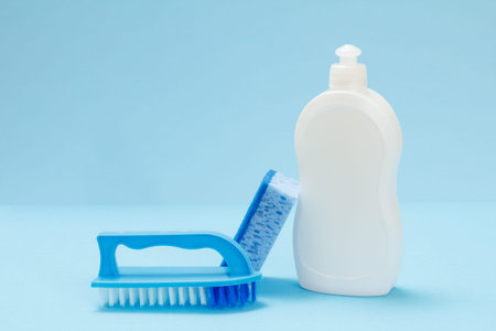 Plastic bottle of dishwashing liquid, a sponge and a brush on the blue background. Washing and...