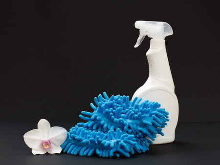 Plastic bottles of dishwashing liquid, a rag and a white orchid flower on the black background....
