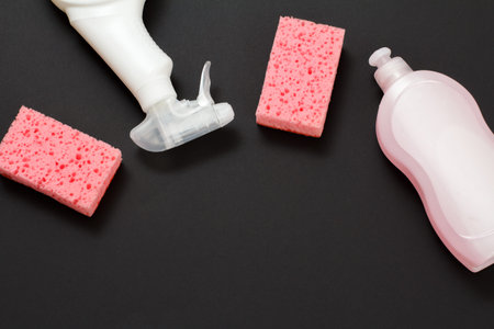 Plastic bottles of washing liquid and sponges on the black background. Top view. Washing and...