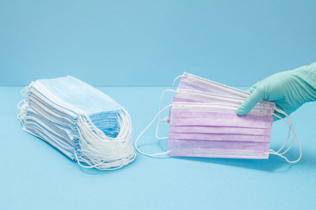 Doctor in a latex glove holding medical protective masks in her hand and a stack of masks on the...