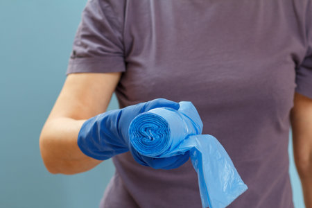Woman in a t-shirt holding garbage bags on the blue background. Shallow depth of field. Focus on...